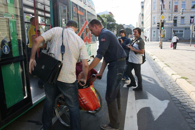Christian Hausmann (ganz links) und Burkhard Lischka (3.v.l.) helfen Andreas Poppe beim Einsteigen in die Straßenbahn Linie 6 in Richtung Diesdorf.